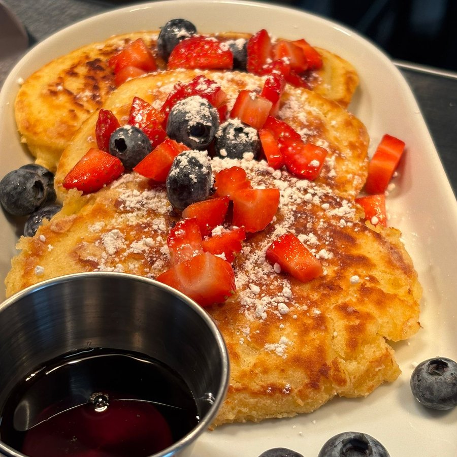 French toast topped with strawberries and blueberries at PadamPadam, with a jug of maple syrup.
