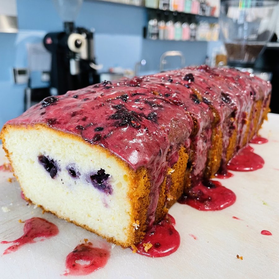 A blueberry loaf cake with a berry glaze, sliced on the counter at PadamPadam.