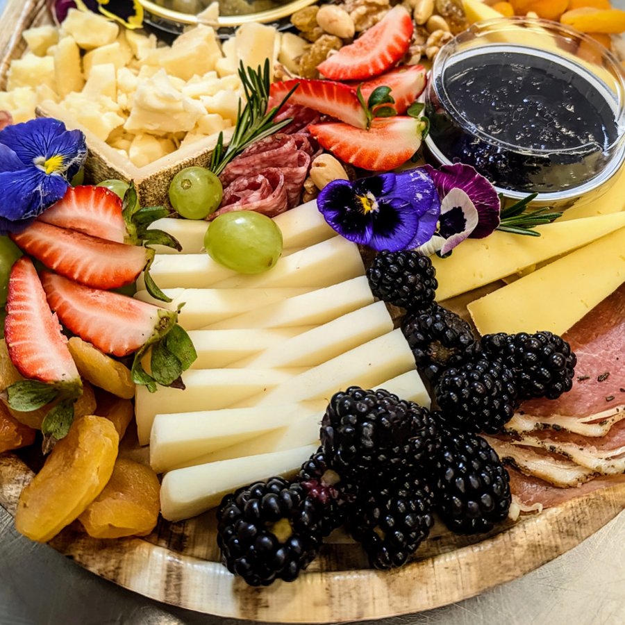 A catering cheeseboard with cheese, charcuterie, fruit and edible flowers, made by PadamPadam.