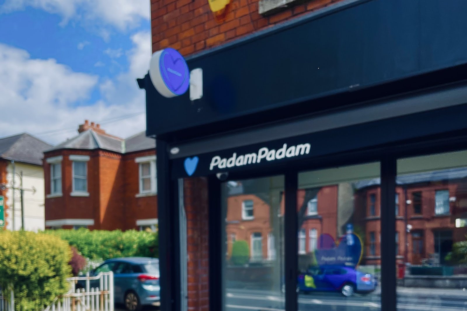 The black PadamPadam shopfront on Drumcondra Road Upper, with its blue heart sign, glass frontage and outdoor tables.