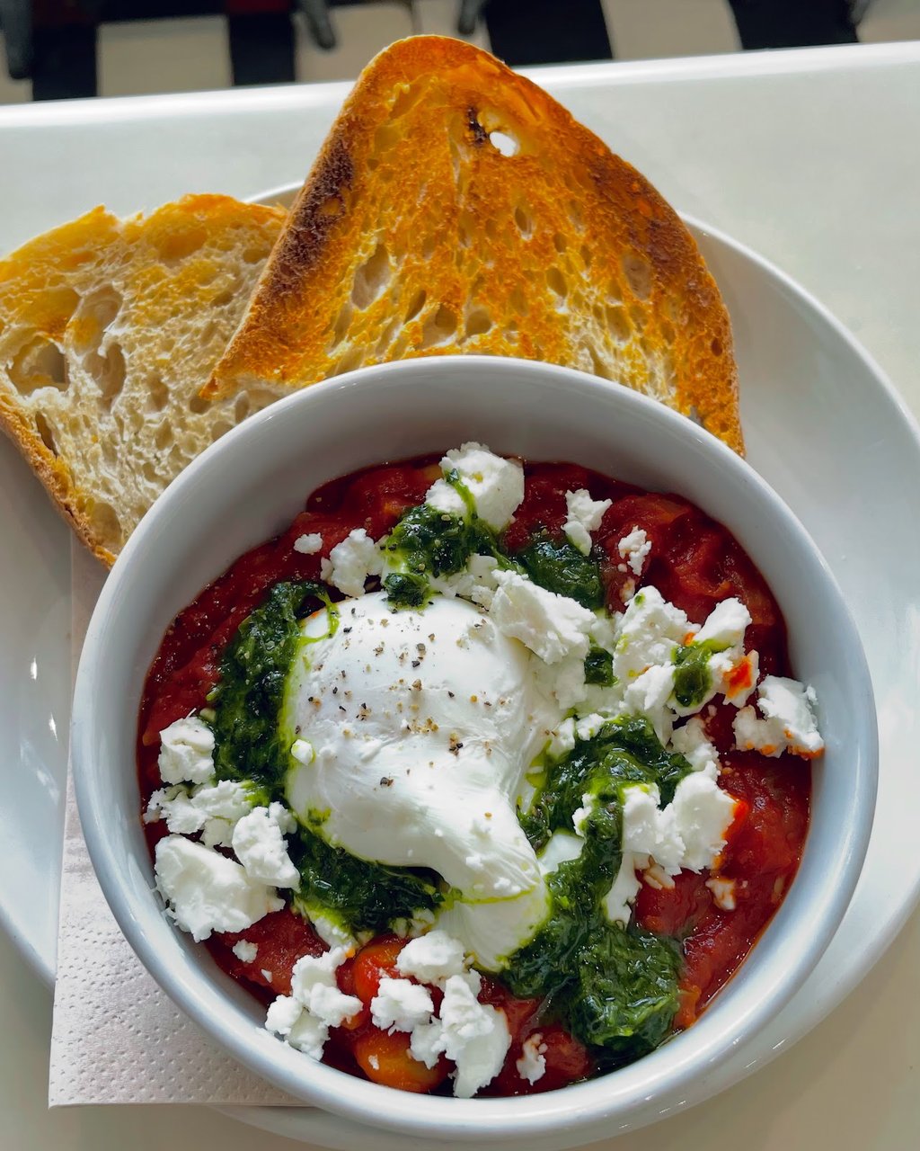 A bowl of baked tomato, feta and poached egg with sourdough toast at PadamPadam.